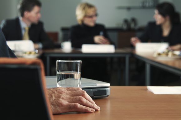 Reunión de negocios con participantes serios y un vaso de agua en la mesa.