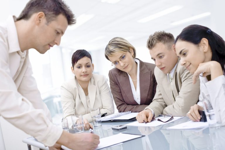 Reunión de cinco profesionales discutiendo y tomando notas en una sala luminosa.