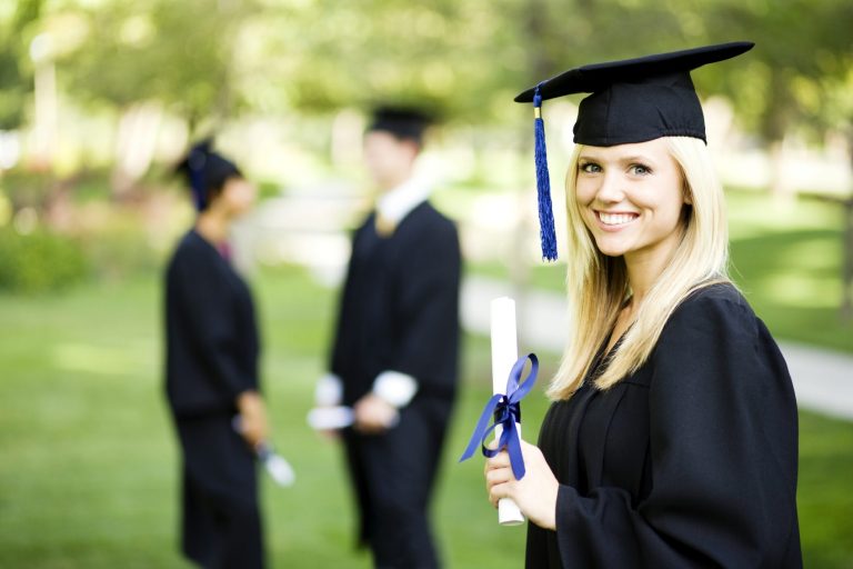 Joven graduada sonriente con toga y birrete sosteniendo un diploma en un entorno al aire libre.
